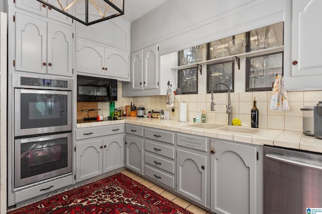 kitchen featuring tile countertops, gray cabinetry, backsplash, sink, and stainless steel appliances