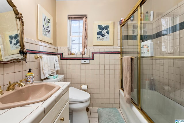 full bathroom featuring vanity, shower / bath combination with glass door, tile patterned floors, toilet, and tile walls