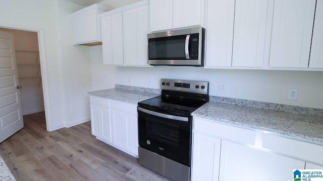 kitchen with light stone countertops, white cabinets, stainless steel appliances, and light hardwood / wood-style floors