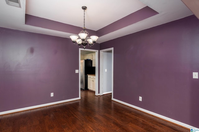 empty room with a tray ceiling, dark hardwood / wood-style flooring, and an inviting chandelier