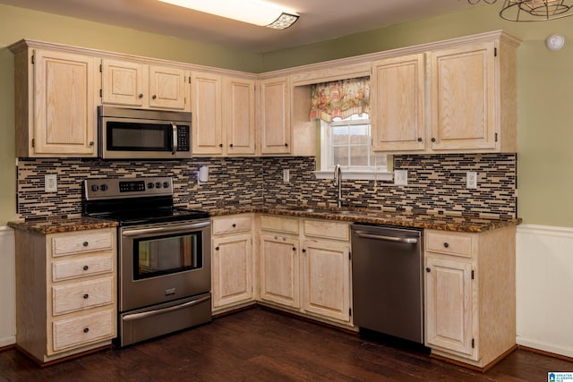 kitchen with appliances with stainless steel finishes, backsplash, dark hardwood / wood-style floors, dark stone countertops, and sink