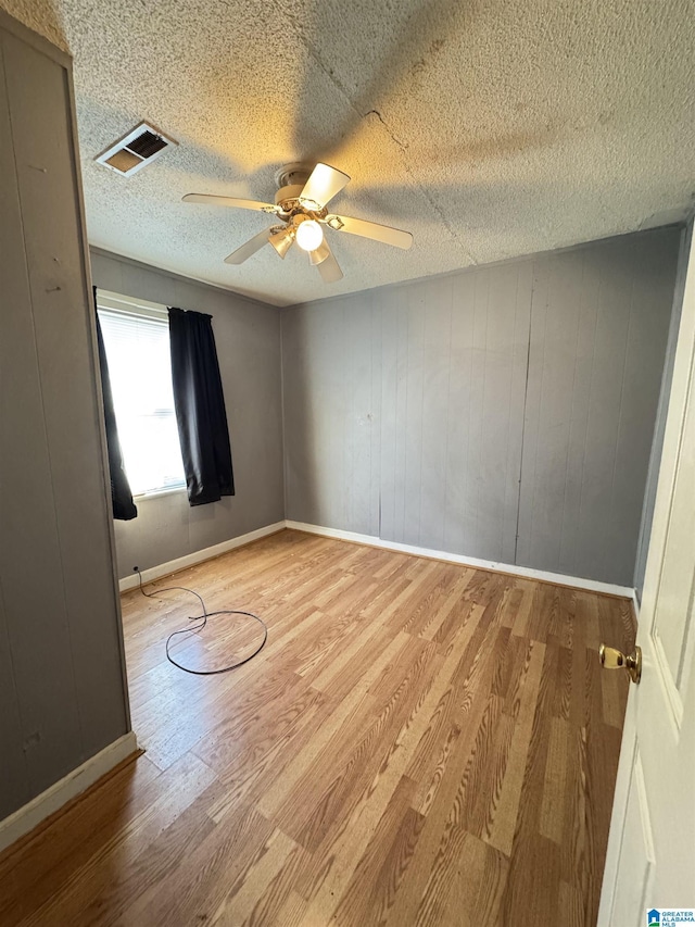 unfurnished room featuring ceiling fan, wooden walls, and light wood-type flooring