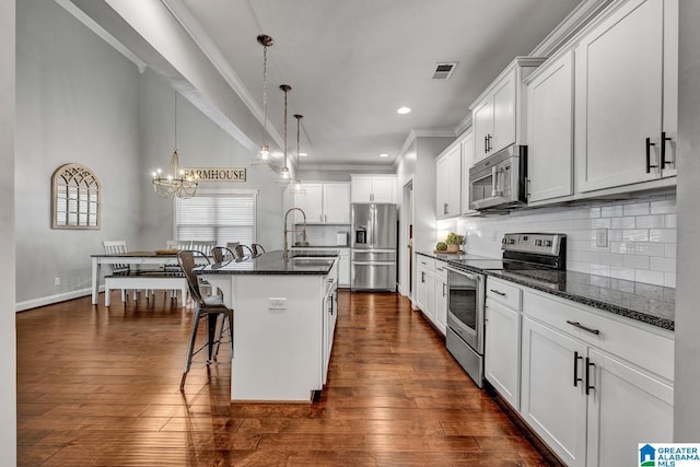 kitchen featuring white cabinetry, a kitchen breakfast bar, dark stone countertops, a kitchen island with sink, and appliances with stainless steel finishes