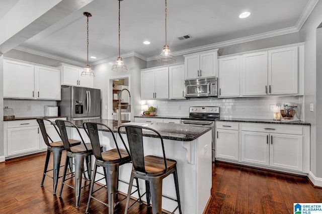 kitchen with a center island with sink, hanging light fixtures, tasteful backsplash, white cabinetry, and stainless steel appliances