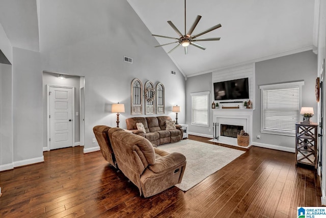 living room with ceiling fan, a large fireplace, dark wood-type flooring, high vaulted ceiling, and ornamental molding