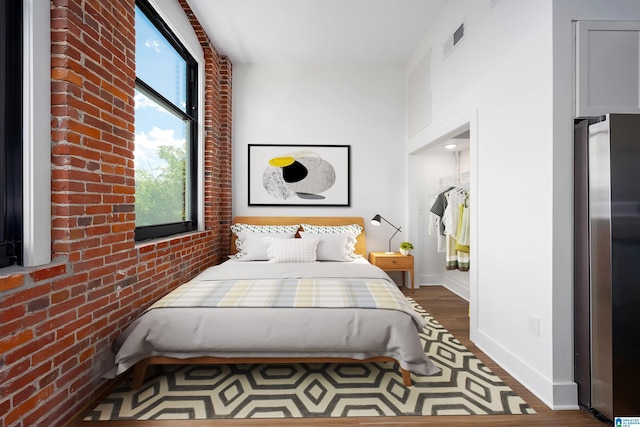 bedroom featuring dark hardwood / wood-style flooring, brick wall, and stainless steel refrigerator