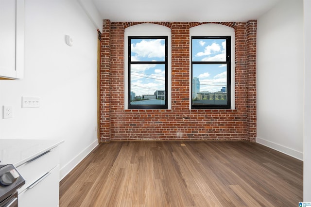 spare room with hardwood / wood-style floors and brick wall