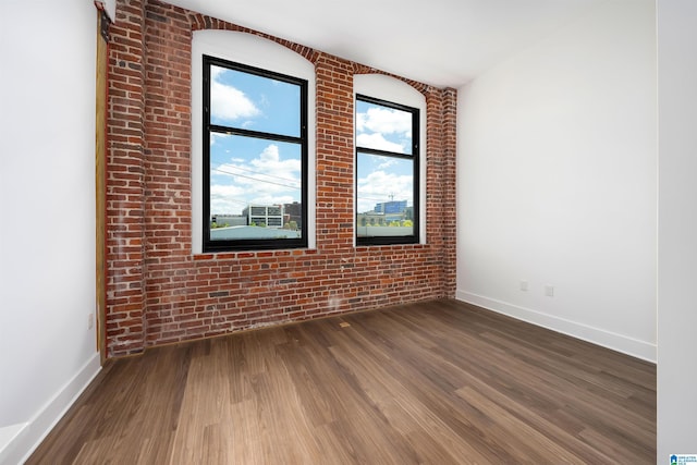 empty room with wood-type flooring and brick wall