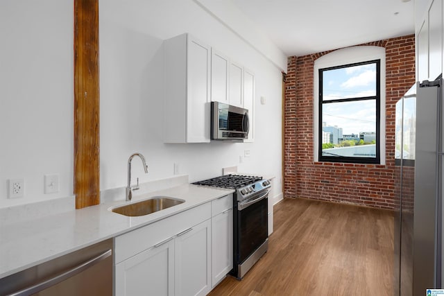 kitchen with white cabinetry, sink, light stone countertops, stainless steel appliances, and brick wall