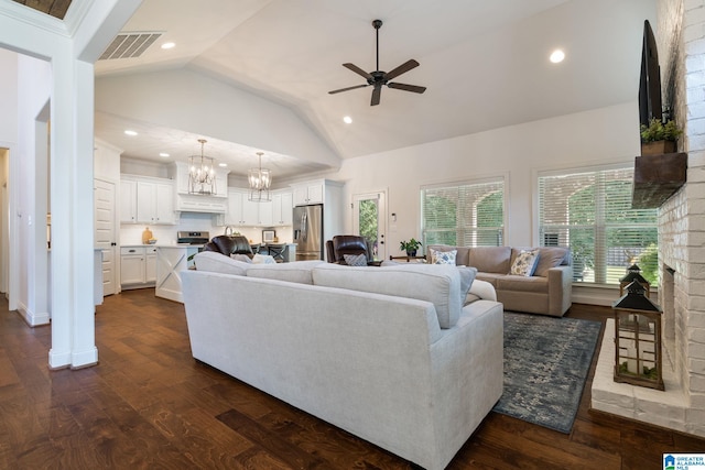 living room with ceiling fan with notable chandelier, a fireplace, dark wood-type flooring, and high vaulted ceiling