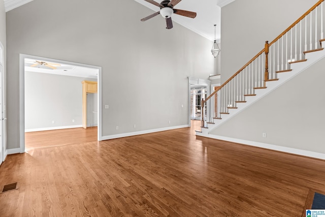 unfurnished living room featuring a towering ceiling, hardwood / wood-style flooring, ceiling fan, and ornamental molding