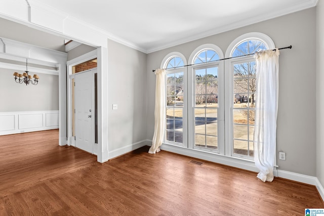 spare room featuring wood-type flooring, crown molding, and a notable chandelier