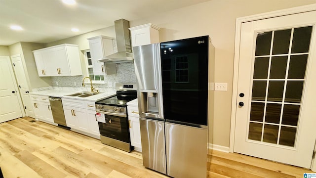 kitchen with sink, wall chimney range hood, tasteful backsplash, white cabinets, and appliances with stainless steel finishes