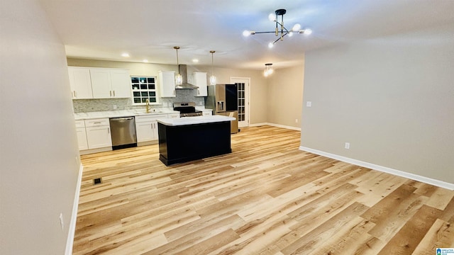 kitchen with appliances with stainless steel finishes, wall chimney range hood, decorative light fixtures, white cabinets, and a kitchen island