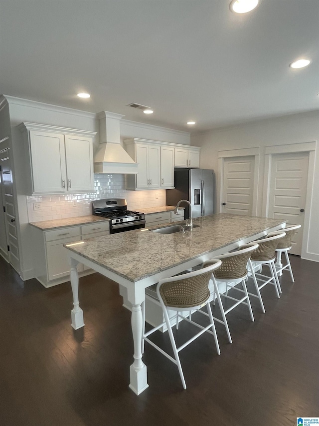 kitchen with a kitchen bar, premium range hood, stainless steel appliances, a kitchen island with sink, and sink