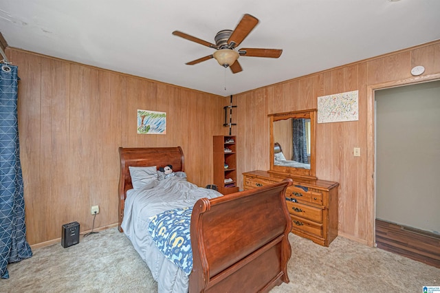 bedroom featuring ceiling fan, wood walls, and light colored carpet