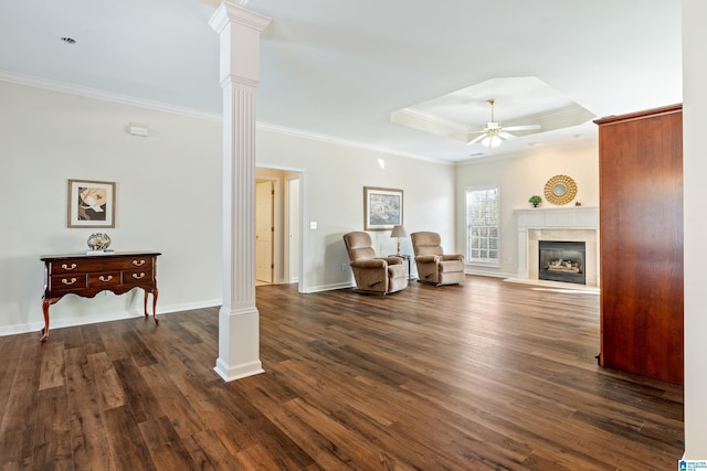 living area with dark hardwood / wood-style flooring, decorative columns, a tray ceiling, and ornamental molding