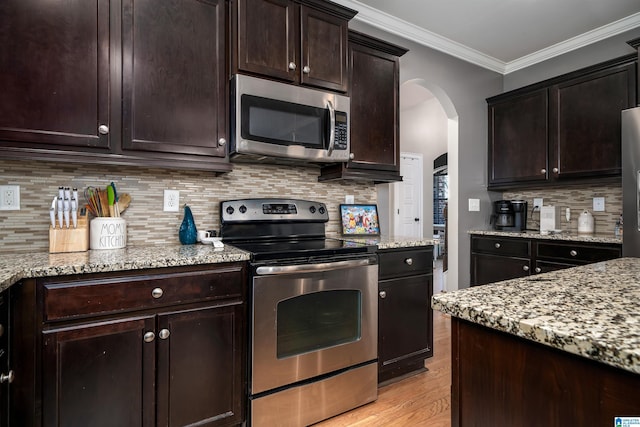 kitchen with appliances with stainless steel finishes, tasteful backsplash, dark brown cabinets, crown molding, and light hardwood / wood-style flooring