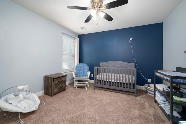 carpeted bedroom with ceiling fan and a crib