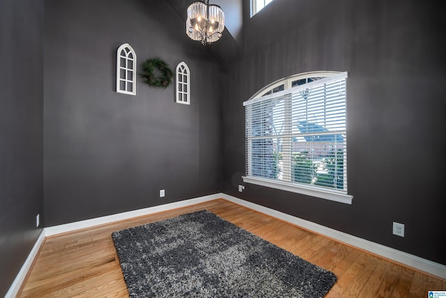 empty room with hardwood / wood-style floors, a high ceiling, and a notable chandelier