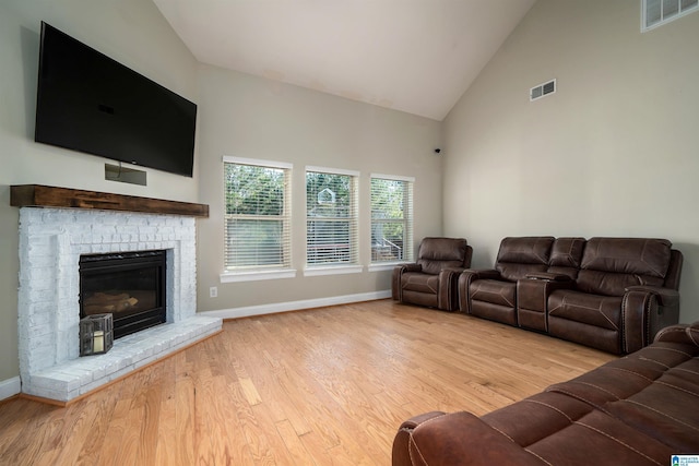 living room with high vaulted ceiling, light hardwood / wood-style floors, and a brick fireplace