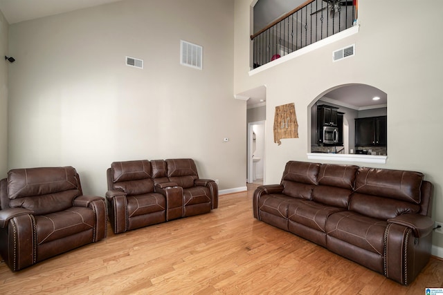 living room featuring wood-type flooring, ornamental molding, and a high ceiling