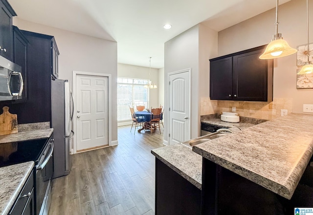 kitchen with kitchen peninsula, appliances with stainless steel finishes, tasteful backsplash, pendant lighting, and light hardwood / wood-style floors