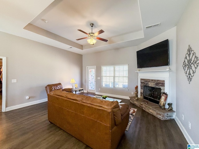 living room with a fireplace, dark hardwood / wood-style flooring, a raised ceiling, and ceiling fan