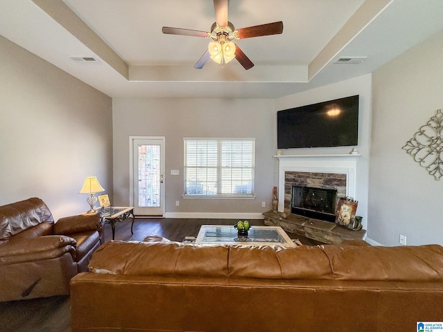 living room with a fireplace, a raised ceiling, ceiling fan, and dark wood-type flooring