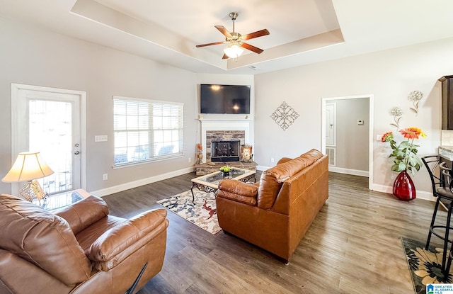 living room with a fireplace, dark hardwood / wood-style flooring, a tray ceiling, and ceiling fan