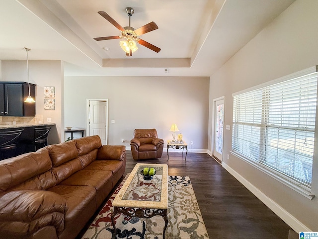 living room featuring dark hardwood / wood-style flooring, ceiling fan, a raised ceiling, and a wealth of natural light