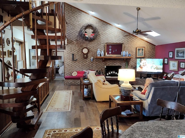 living room featuring lofted ceiling with skylight, hardwood / wood-style flooring, ceiling fan, a textured ceiling, and brick wall