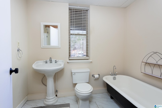 bathroom featuring toilet, marble finish floor, baseboards, and a freestanding bath