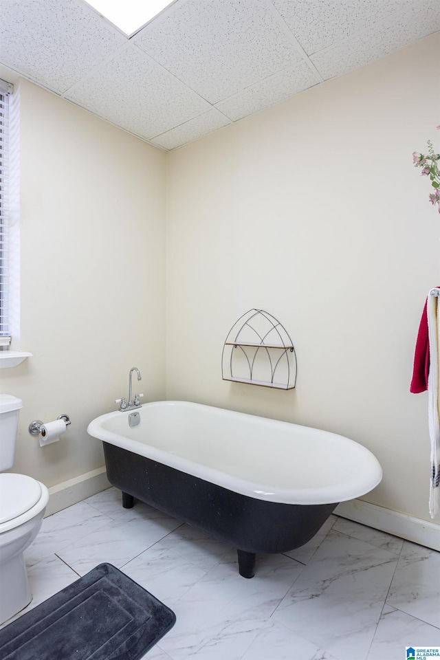 full bath with marble finish floor, baseboards, a soaking tub, and toilet