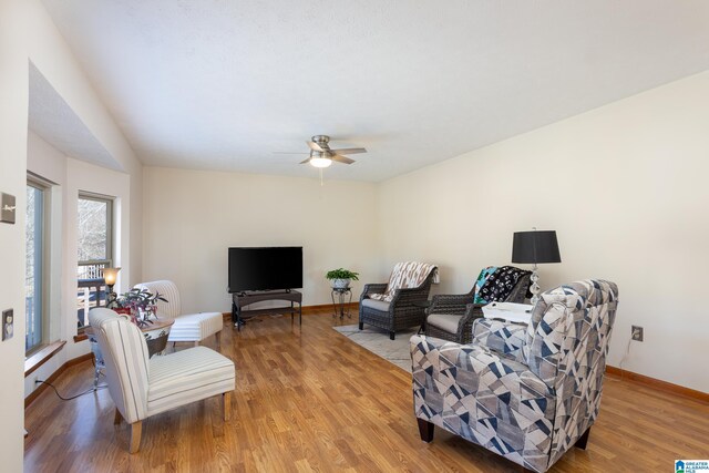 living area with baseboards, ceiling fan, and light wood finished floors