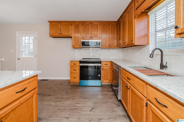 kitchen with light stone countertops, appliances with stainless steel finishes, tasteful backsplash, sink, and hardwood / wood-style floors