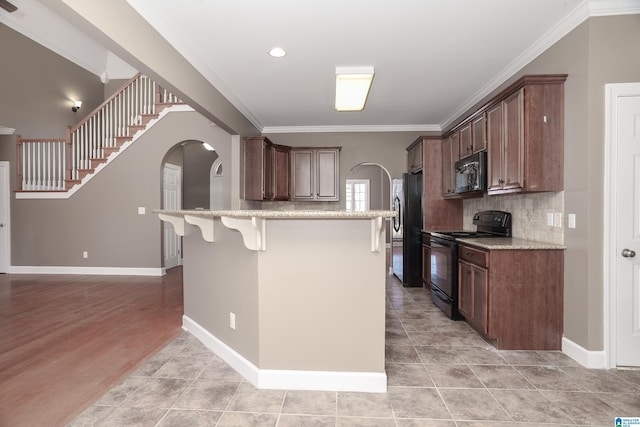 kitchen with backsplash, black appliances, ornamental molding, an island with sink, and a breakfast bar area