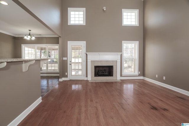 unfurnished living room featuring a fireplace, a high ceiling, dark wood-type flooring, and a notable chandelier