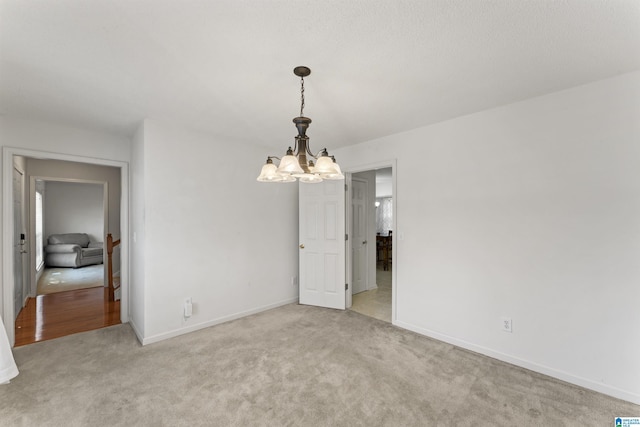 spare room featuring light colored carpet and a notable chandelier