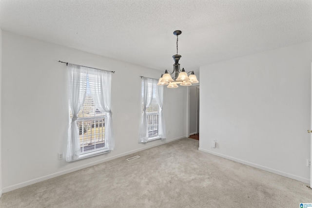 empty room featuring carpet, a textured ceiling, and an inviting chandelier