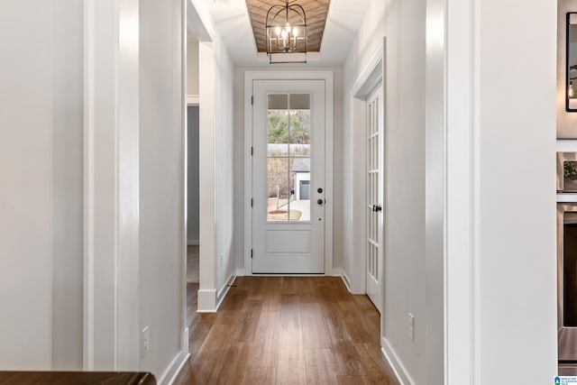 doorway to outside with a raised ceiling, hardwood / wood-style flooring, and a notable chandelier