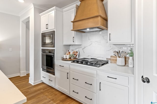 kitchen with custom exhaust hood, white cabinets, light hardwood / wood-style flooring, tasteful backsplash, and stainless steel appliances