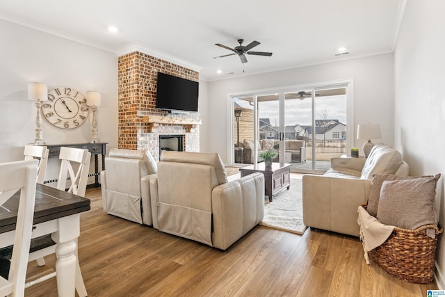 living room with hardwood / wood-style flooring, ceiling fan, ornamental molding, and a brick fireplace