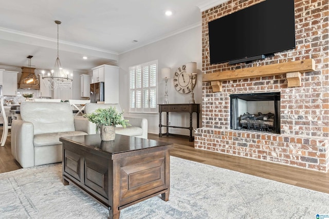 living room with a notable chandelier, light hardwood / wood-style floors, crown molding, and a brick fireplace