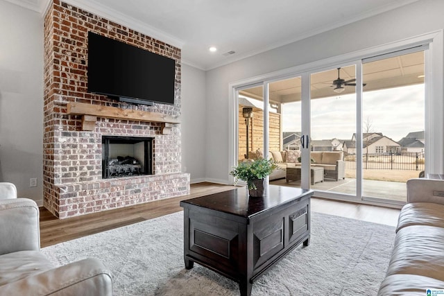 living room featuring hardwood / wood-style floors, ceiling fan, ornamental molding, and a brick fireplace