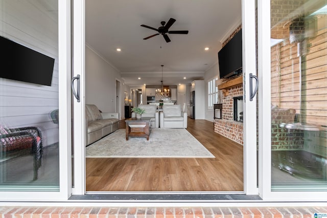 unfurnished living room with ceiling fan with notable chandelier, wooden walls, a brick fireplace, ornamental molding, and dark hardwood / wood-style flooring