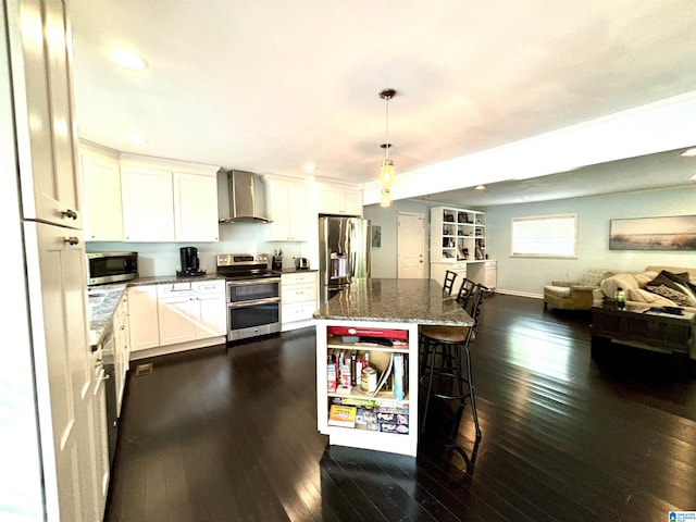 kitchen with wall chimney exhaust hood, a kitchen island, dark stone countertops, white cabinets, and appliances with stainless steel finishes