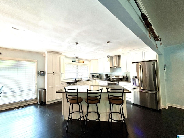 kitchen featuring appliances with stainless steel finishes, wall chimney exhaust hood, sink, pendant lighting, and a center island