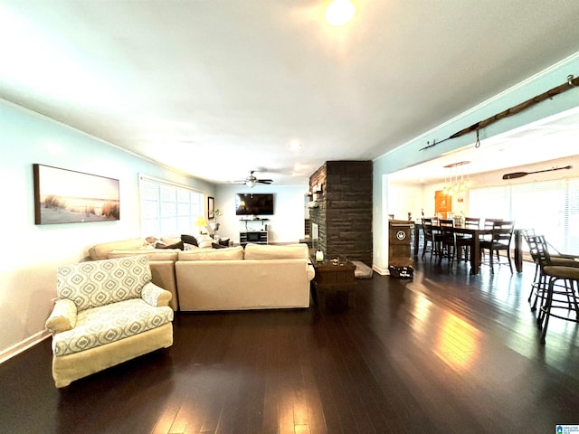 living room with a stone fireplace, ceiling fan, dark hardwood / wood-style flooring, and plenty of natural light