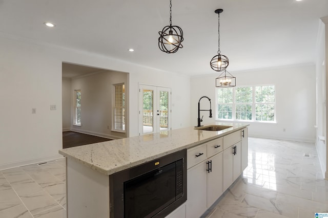 kitchen featuring built in microwave, sink, pendant lighting, a center island with sink, and white cabinets